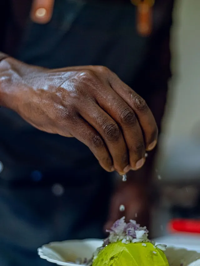 A chef's hand seasoning a dish