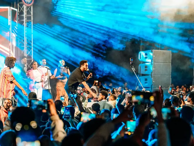 A band performs on a lit stage as the crowd holds up their phones
